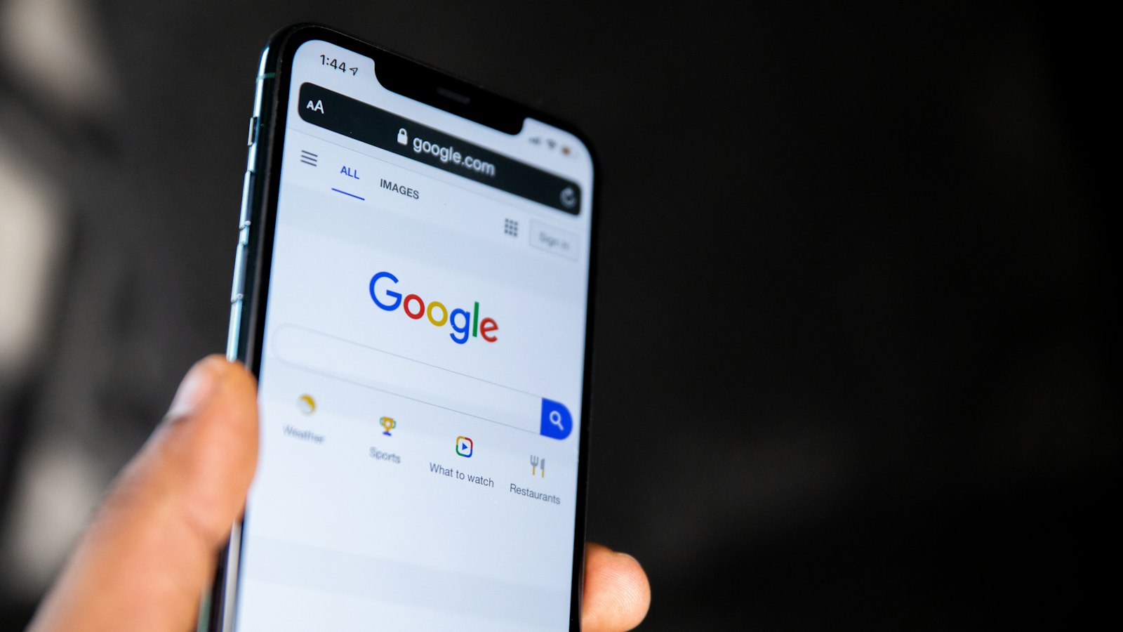 Hand holding a smartphone showing Google Search, where AI Mode and AI Overviews now answer local questions